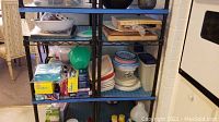 Photo of metal shelves with assorted kitchen items including plastic containers, wooden boards, and a dry fry pan