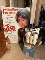 Full view of framed Tom and Huck movie poster standing upright beside a box of rolled posters.