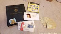 US First Day Covers black binder, assorted envelopes with stamps, coin in protective cover, Richie Rich money clip, and MLB stamps sheet on floor.