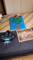 Full view of all three pieces: tree painting on canvas in square format, diamond-shaped metal night sky art, and framed beach rock photograph.