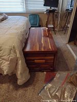 Front perspective of cedar chest next to bed showing exterior finish, lid closed