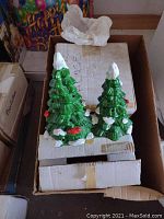 Two green evergreen trees with white snow accents and red berries in a box.