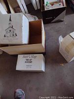 Boxes of Dept 56 Snow Village series items including New England Village, Tree Lot accessory, and large single tree boxed separately.