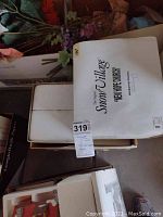 Three white original boxes labeled with Dept 56 Snow Village names including New Hope Church, Fisherman's Nook, and Bakery, stacked and partially opened showing styrofoam interior packaging.