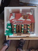 Pinewood Log Cabin ceramic building in original styrofoam packaging inside a box, showing snowy roof and decorated porch columns.