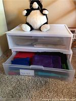 Full front view of the plastic storage bins with fabric inside the bottom drawer and the fat cat plush sitting on top.