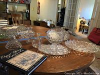 Table with multiple glassware pieces including cake stands, candle holders, relish dish and other decorative glassware