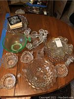 Overview photo of various glassware pieces including bowls, candle holders, and decorative dishes arranged on a wooden table.