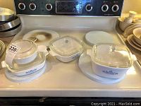 Four Corningware casserole dishes with lids arranged on stove top, white ceramic with blue floral design