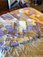 Patchwork quilt laid on bed showing patch patterns and some edge wear.