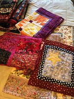 Four small quilted wall hangings displayed on a bed showing different fabrics and patterns.