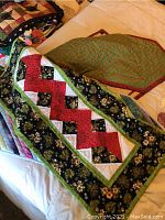 Four folded small patchwork quilts or wall hangings stacked, showing mostly the top piece with red zigzag and green border on floral fabric.