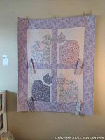 Full view of purple quilted wall hanging with four floral fabric cats and heart appliques on a purple background, displayed hanging on wall.