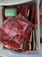 Box with assorted folded Christmas themed quilting fabrics in red, white, and green patterns with a bar of Irish Spring soap for scale