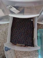 Open plastic drawer showing a stack of folded quilting fabric with small red and beige dot pattern on dark background