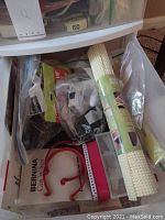 Plastic storage container with quilting tools, including a rolled mesh stabilizer and some packaged items