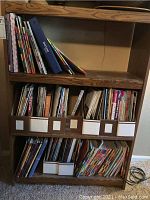 Wooden shelving unit holding a large quantity of quilting magazines and periodicals organized in plastic holders and loose stacks