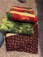 Three folded quilts stacked, showing red Christmas fabric, green snowflake fabric, and maroon floral fabric.