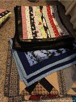 Stack of three quilts showing various folded patterns and colors on carpet.