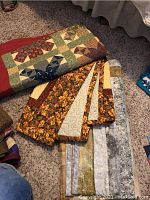 Photo showing three folded quilts on carpet, displaying patchwork designs with autumn colors and floral prints.