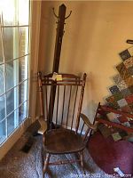 Front view of wooden rocking chair and coat tree side by side against wall next to glass door