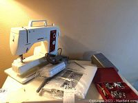 White Bernina Sport 801 sewing machine on base with foot pedal, power cord, packaged stitch regulator and red case of presser feet visible.