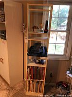 Front view of tall white bookshelf showing cookbooks on bottom shelves, small decorative items and trays on middle shelves.