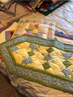 Photo showing two quilted patchwork runners with geometric design in green, yellow, and blue on a light bedspread