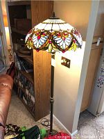 Full view of the floor lamp showing the stained glass shade lit and the dark metal base.