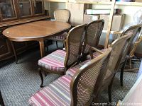 Photo showing the dining table with six chairs arranged around it, highlighting the wood finish, caned backs, and striped upholstery.
