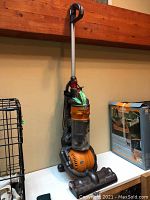 Full front view of the Dyson Ball vacuum showing the orange ball base, clear dust bin with some visible dust, black hose, vacuum head on the floor, and silver handle with trigger style grip.