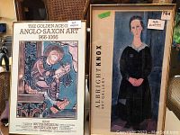 Two framed prints leaning against chairs showing the Albright Knox art print and British Museum exhibition poster.