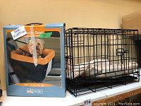 Dog crate with white sleeping pad inside, metal wire construction, shown alongside Kurgo booster seat box