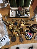 Top-down image showing brass military buttons scattered on the table along with various pins, badges and a British Columbia cloth badge patch.