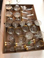 Box showing multiple wine glasses with gold rims, viewed from top and side angles.