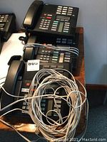 Four black Meridian desk phones stacked, showing keypads, function buttons, and coiled cords with extra phone cord on top.