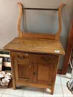 Light wood washstand, frontal view showing drawer, cabinet doors, and curved towel bar supports with missing towel bar attachment.