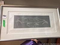 Full view of abstract Native Art print framed in silver. Six stylized figures forming a ring dance pattern in white on gray background with embossed white border.