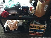 Overall view of shelf with fabrics, knitting needles, boots, T-shirts in bag, bathrobes, apron in bag, and other items.