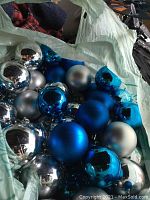 Close-up photo of assorted Christmas ball ornaments in blue, silver, and metallic blue finishes inside a plastic bag.