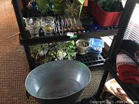 Photo of large plain steel basin and garden decor on shelving including pots, flowers, and small containers with garden rocks.
