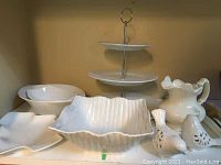 Photo showing several white ceramic serving dishes including a large ridged square dish, a two-tiered serving tray, a pitcher with ornate spout and handle, and bird-shaped salt and pepper shakers.