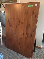 Photo of solid wood rectangular dining table top propped upright against a wall showing wood grain and surface condition.