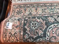 Close-up of edge corner showing dusty rose colored wool area rug with detailed floral and geometric patterns, some dust visible.