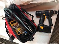 Open red/black tool bag showing hand tools and drill bits next to cordless drill