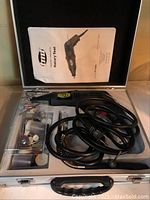 Photo of open carrying case showing the rotary tool with attached cord, flexible shaft, and organized bits in clear plastic compartments.