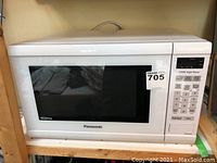 Front view of white Panasonic microwave oven on wooden shelf with Maxsold tag visible