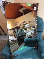 Front view of the rectangular mirror resting on a blue upholstered chair, showing clear reflective surface and decorative metal corners.