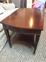Single end table showing dark wood grain, rectangular top with glass insert, tapered legs, and lower curved shelf