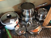Overview of lot showing white Hitachi Chime-O-Matic slow cooker on left and stainless steel Lagostina Commercial Pro cookware pieces stacked on right